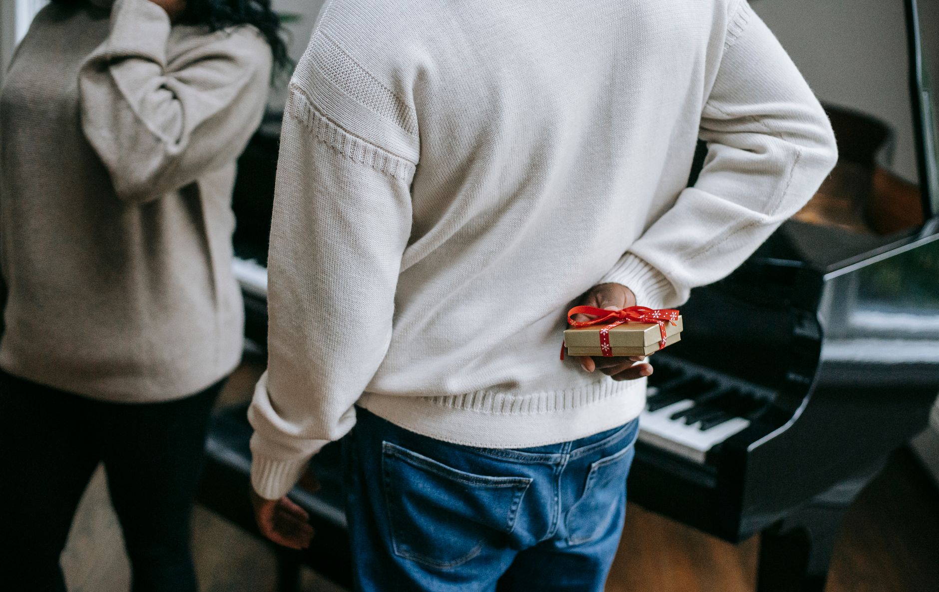 Gift buyer holding a wrapped present behind their back next to a piano
